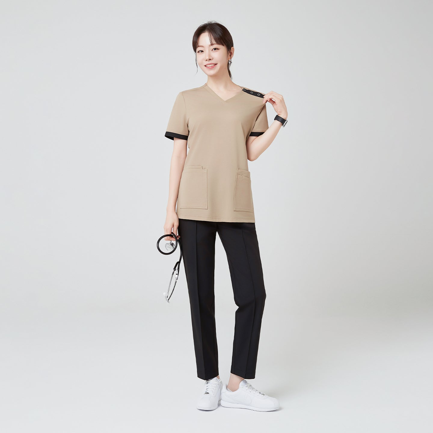 Image of Standing with a bright smile, the model in Sand Beige OS-229 showcases the scrub’s clean silhouette and contrasting black accents that add a polished, modern touch.