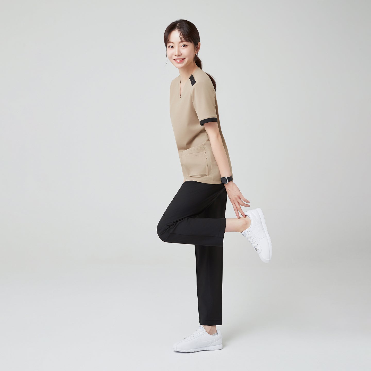 Image of With a playful stretch and a bright smile, the model in Sand Beige OS-229 highlights the scrub’s flexibility and comfort, perfect for active, all-day wear.