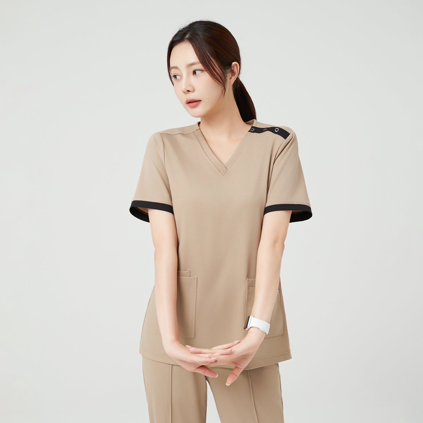 Standing with hands gently clasped in front, the model in Sand Beige OS-229 gives a calm, composed impression, emphasizing the clean lines and relaxed structure of the scrub.