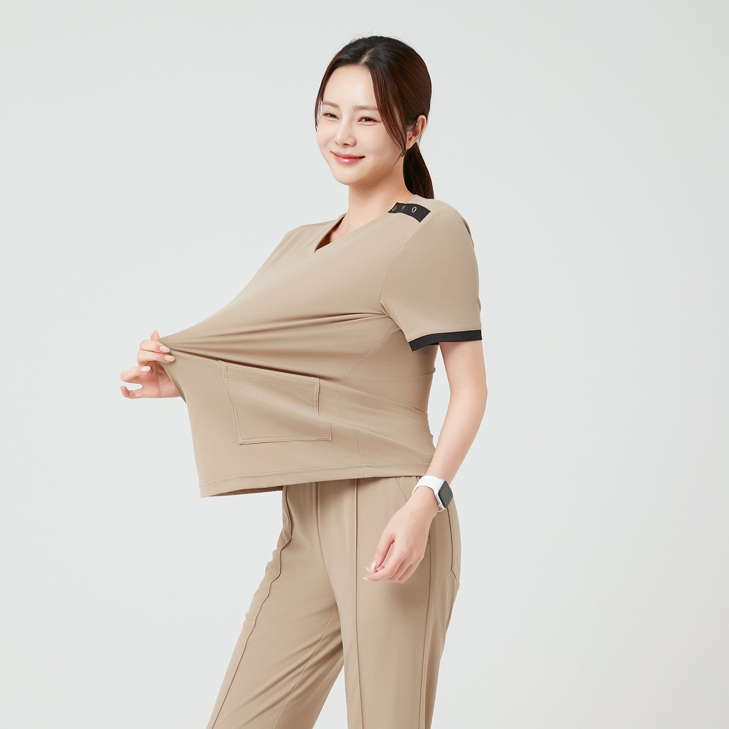 Image of The model gently stretches the fabric to demonstrate its flexibility, highlighting the comfortable elasticity and resilience of the Sand Beige OS-229 scrub.
