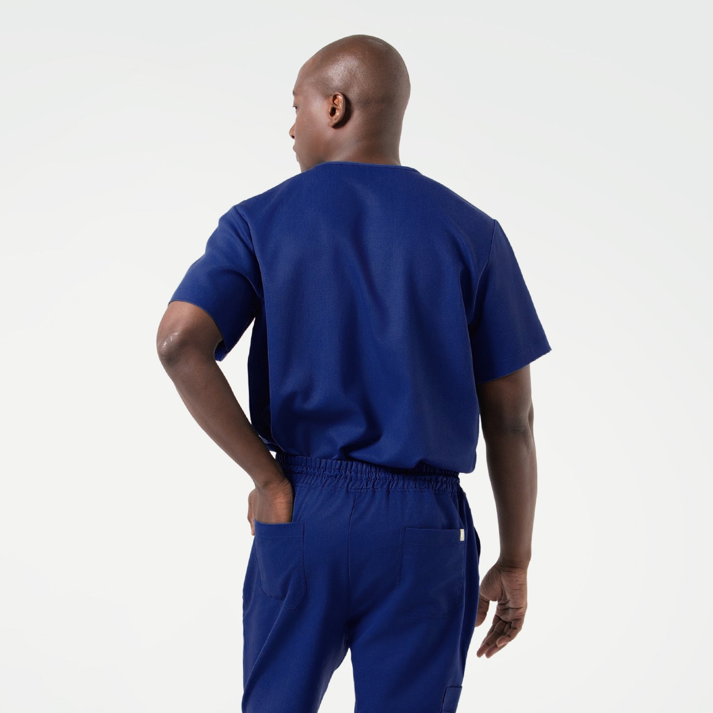 Image of Back view of a model wearing the Admiral Blue Zenir double-pocket scrub top, highlighting the relaxed fit, smooth seams, and comfortable short-sleeve design.