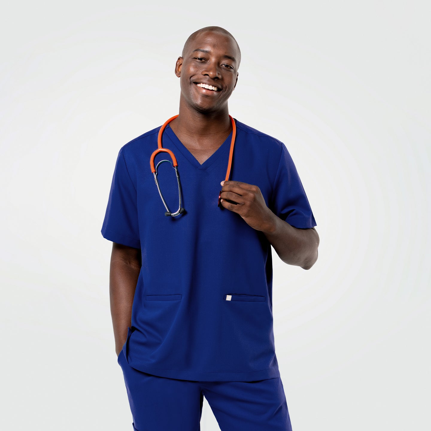 Image of The Admiral Blue Double Pocket Scrub Top styled on a model holding the stethoscope with one hand.