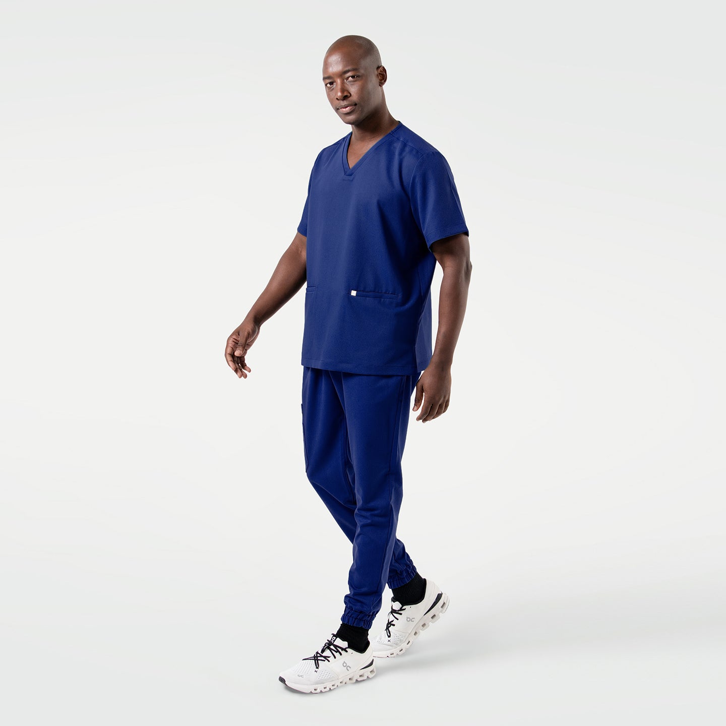 Image of Model wearing Zenir’s Admiral Blue double-pocket scrub top, captured mid-step to highlight the flexible fabric, relaxed fit, and practical front pockets.