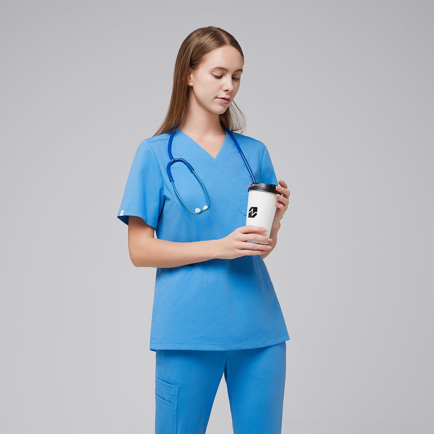 Woman wearing an aqua blue scrub top and pants, holding a coffee cup with a stethoscope around her neck, standing in a calm and composed pose,Aqua Blue