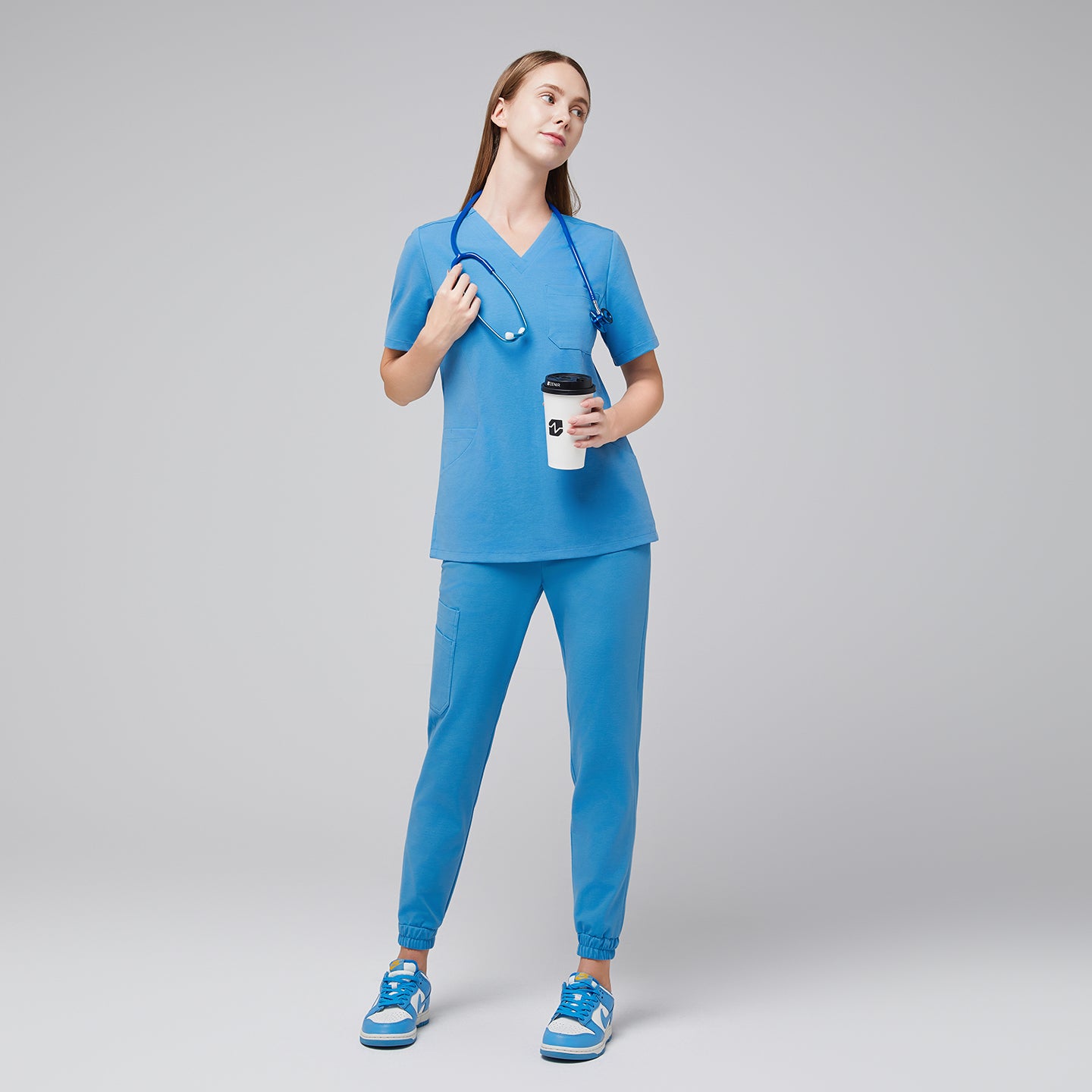 Woman wearing an aqua blue scrub set, holding a coffee cup and stethoscope, standing in a relaxed pose with matching blue sneakers,Aqua Blue