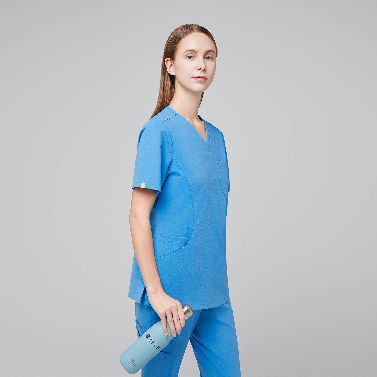 Woman wearing an aqua blue scrub top and pants, holding a matching Zenir-branded water bottle, standing in a side pose with a confident expression,Aqua Blue