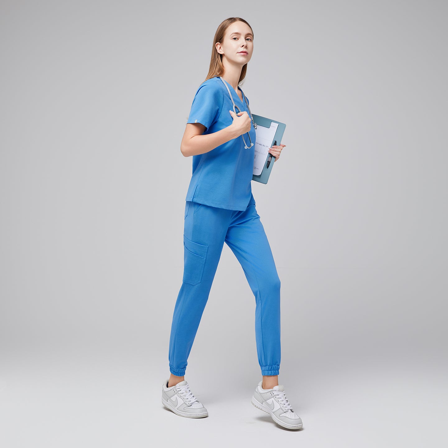 Image of Side view of a woman in aqua blue jogger scrubs holding a clipboard and stethoscope, wearing white sneakers,Aqua Blue