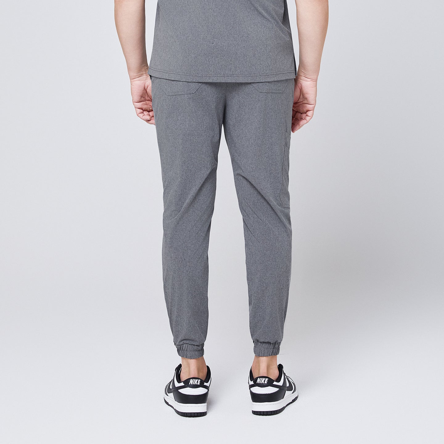 Image of Back view of ash gray jogger scrub pants with elastic cuffs and back pockets, styled with black and white sneakers,Ash Gray