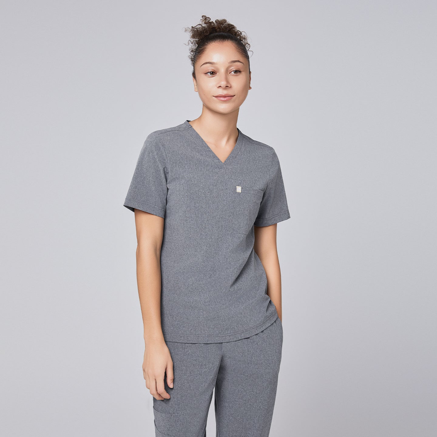 Female healthcare professional wearing an ash gray scrub top and pants, standing with hands casually in pockets,Ash Gray
