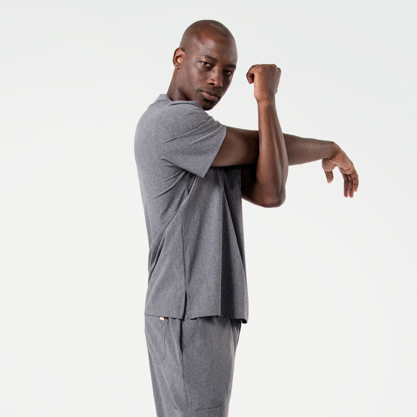 Image of Stretching his arm across his chest, the male model wears an Ash Gray scrub set, combining a sense of movement with a professional look.