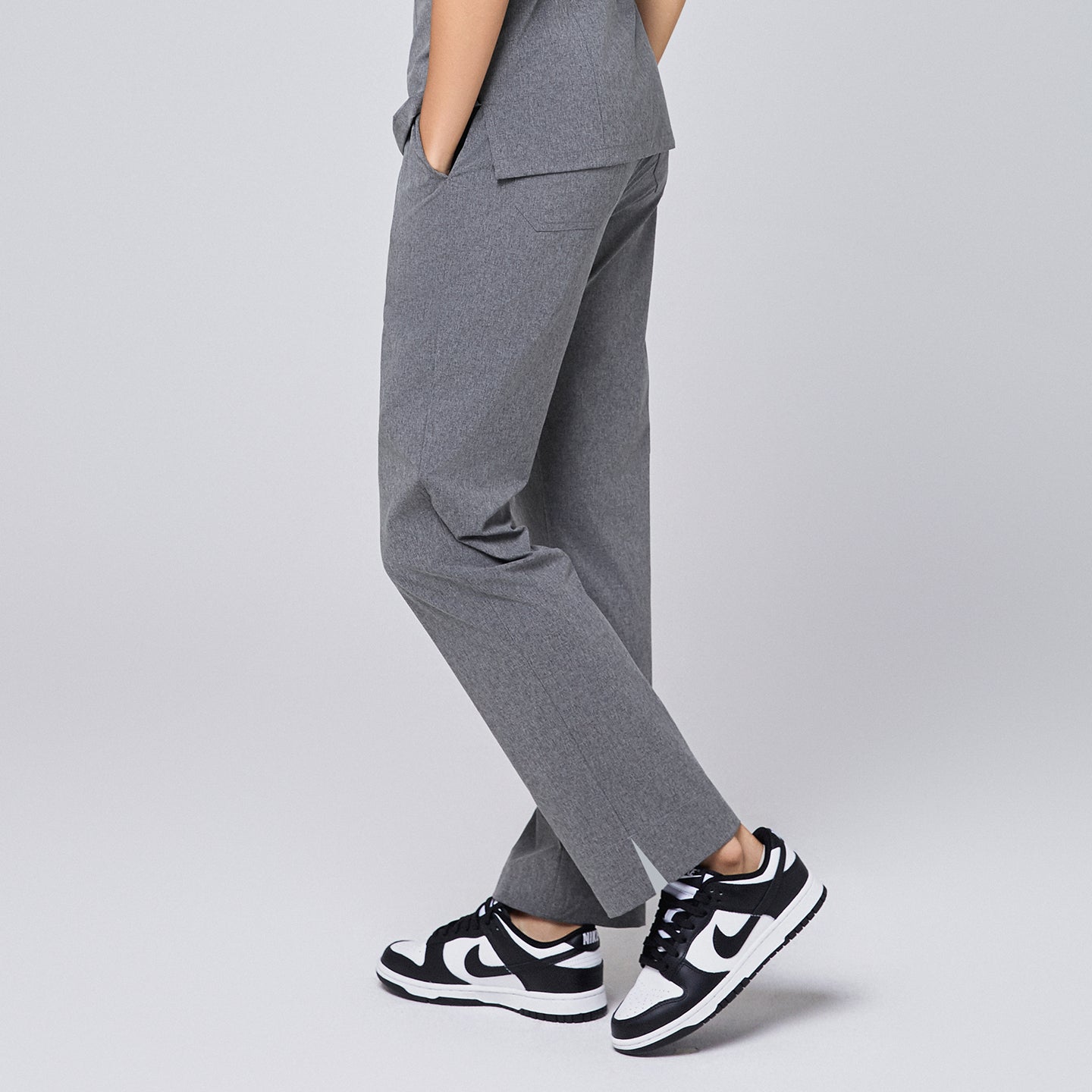 Image of Side view of ash gray straight-leg scrub pants with a split hem and pockets with black sneakers on, highlighting the clean and professional design,Ash Gray