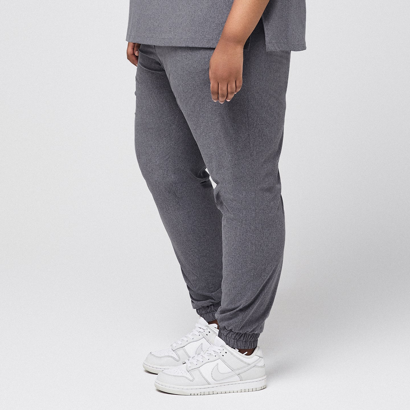 Image of Side angle of ash gray jogger scrub pants with a stretch fit, elastic cuffs, and white sneakers, designed for plus-size comfort,Ash Gray
