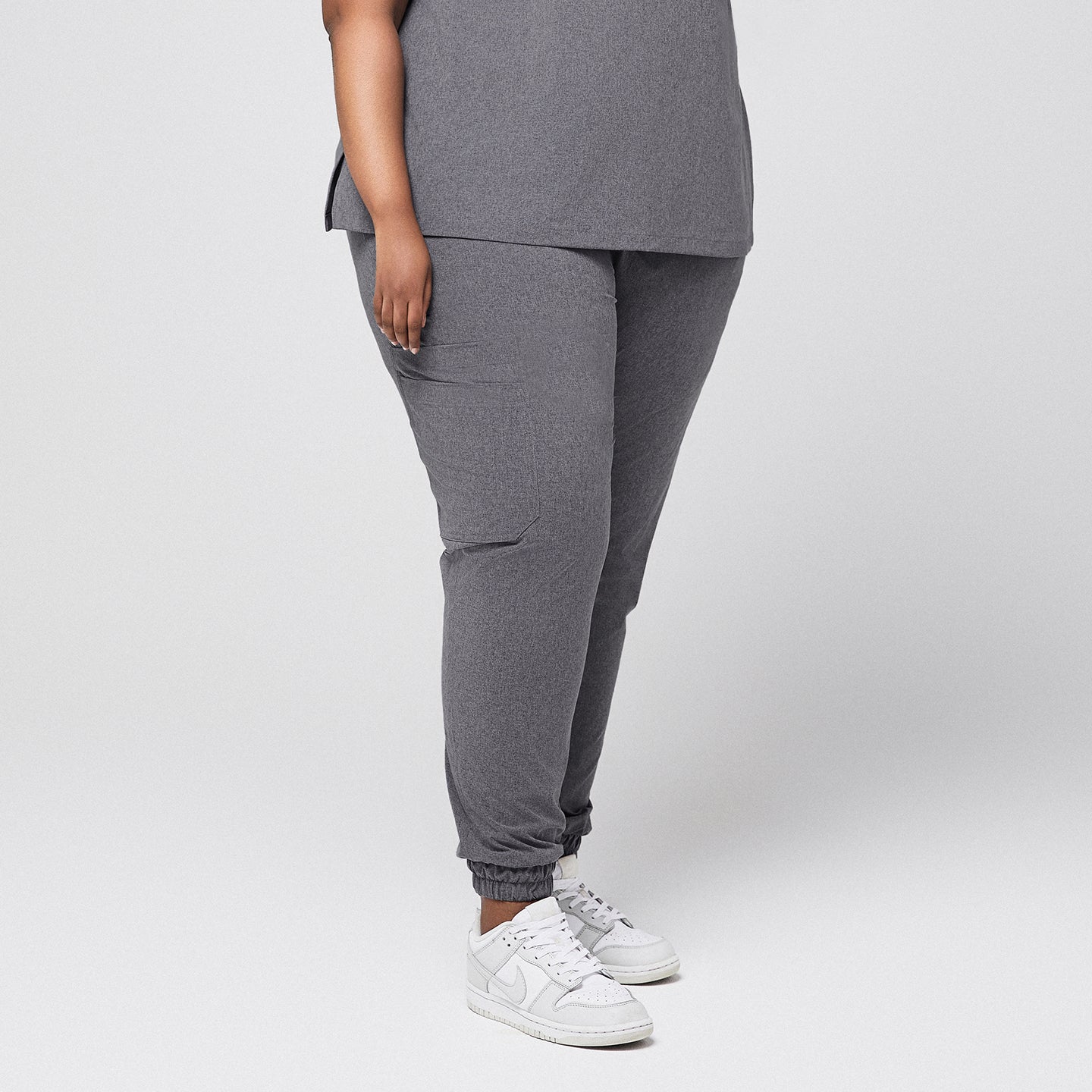 Image of Side view of ash gray jogger-style stretch-fit scrub pants with a cargo pocket, elastic cuffs, and white sneakers,Ash Gray