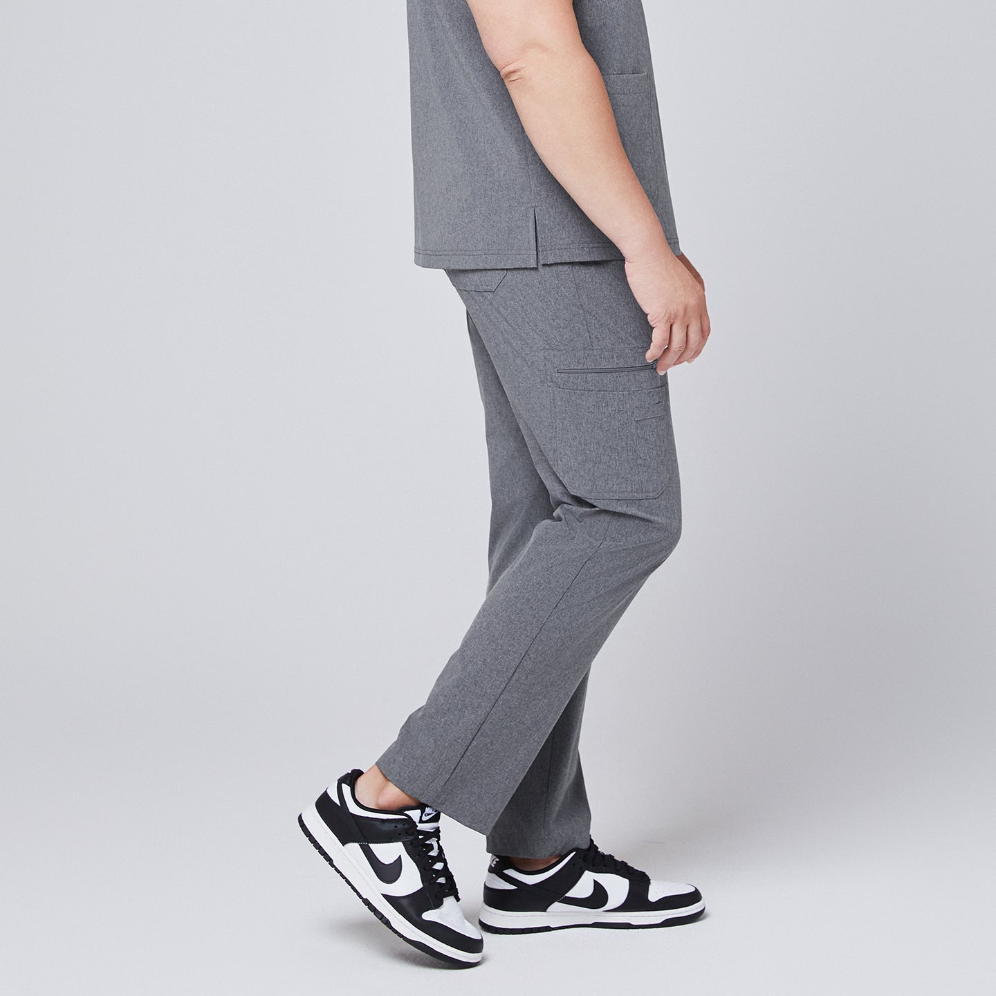 Image of Male model showcasing ash gray relaxed-fit scrub pants with functional side pockets, styled with black and white sneakers, highlighting a side profile for a sleek and professional look,Ash Gray