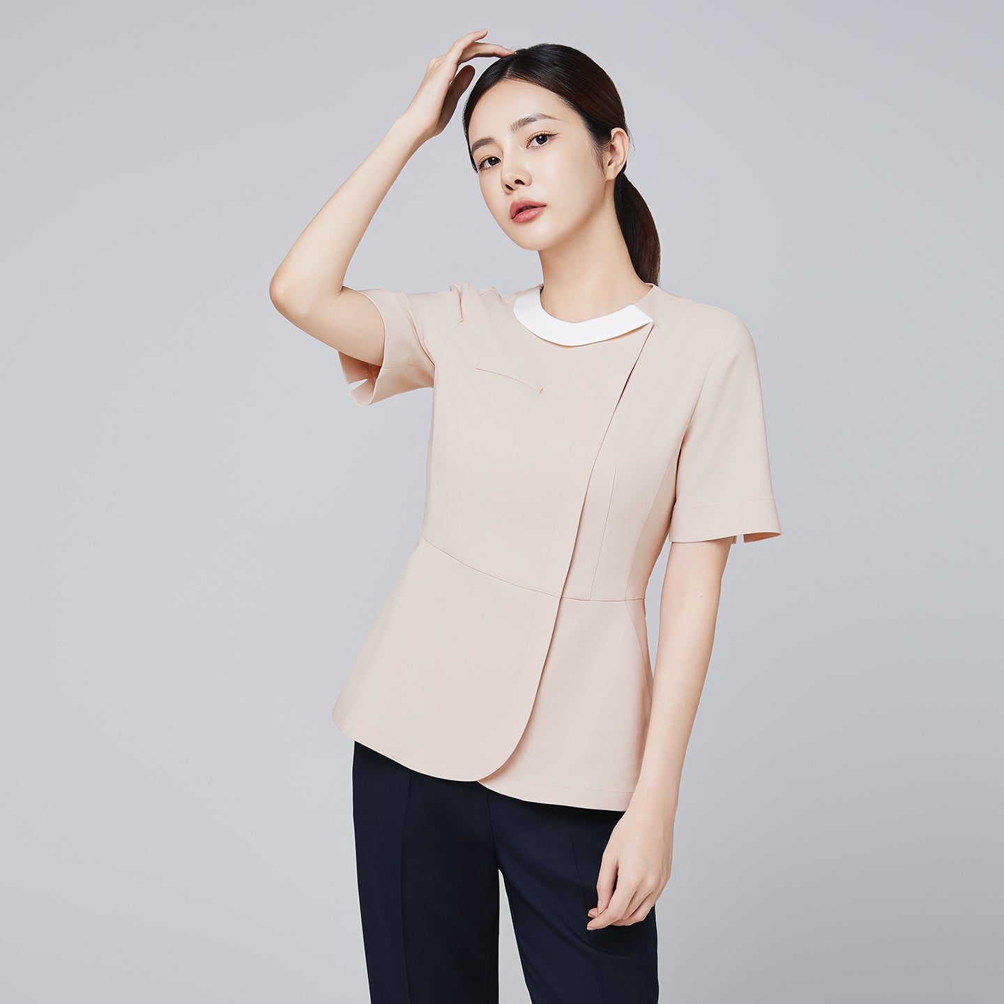 Image of Model wearing TUL NS-149 Women's Round Collar Front Zipper Scrub Top in Beige, highlighting a contrasting white collar and fitted waist.