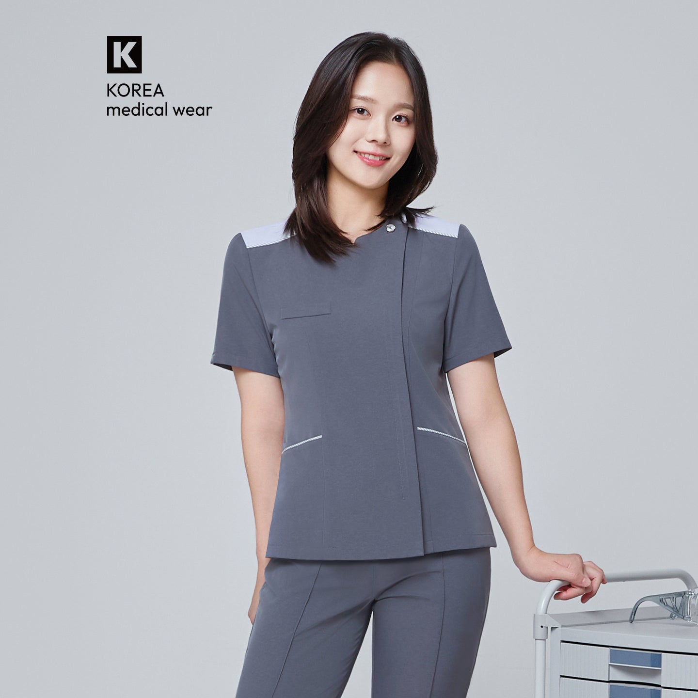 Image of Front view of TUL OS-202 Women's One Button Front Zipper Scrub Top in Blue Gray on a model, showcasing a one-button closure at the chest and a full-length front zipper on a sleek, tailored silhouette.