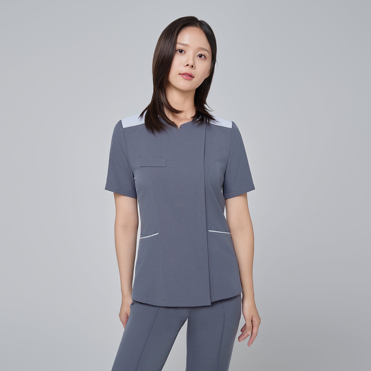 Model wearing TUL OS-202 Women's One Button Front Zipper Scrub Top in Blue Gray, paired with matching scrub bottoms, displaying a cohesive, modern uniform ideal for healthcare settings.