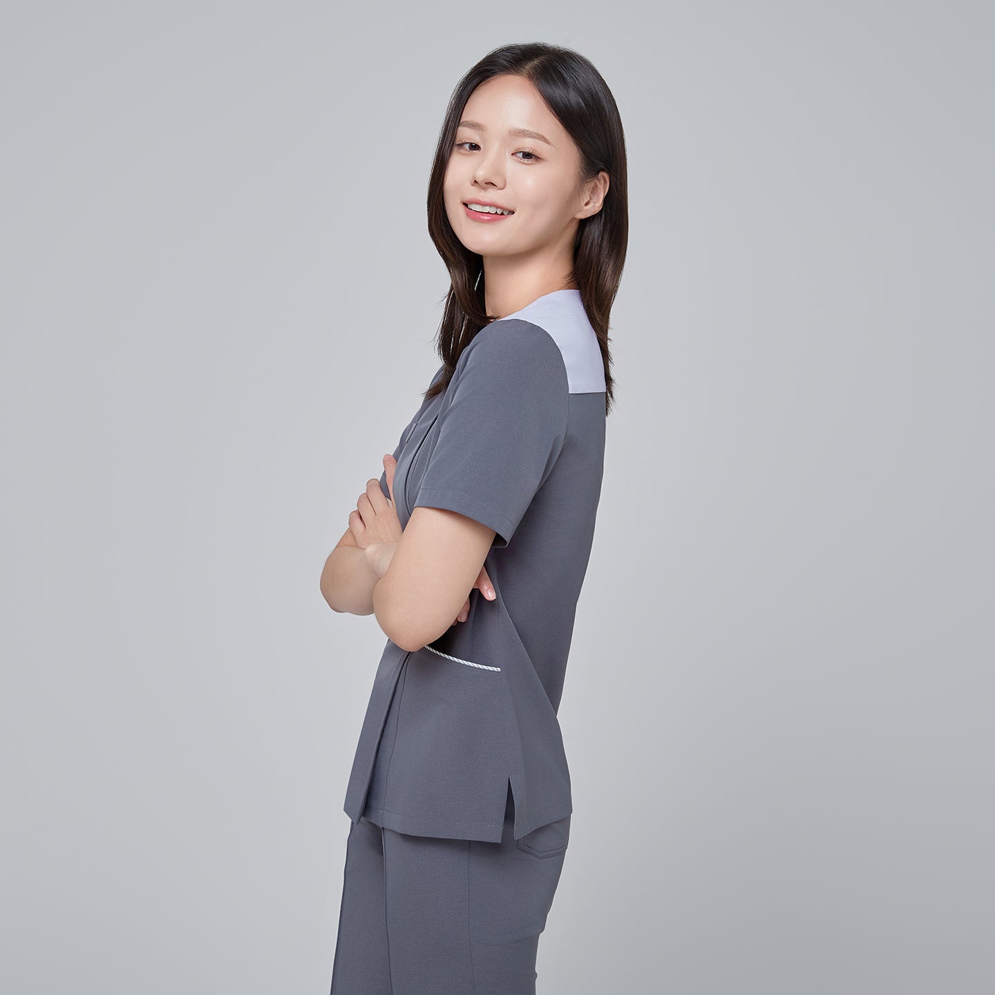 Side angle of TUL OS-202 Women's One Button Front Zipper Scrub Top in Blue Gray worn by a model, highlighting the smooth fabric drape, slim fit, and design details of the one-button and zipper closures.