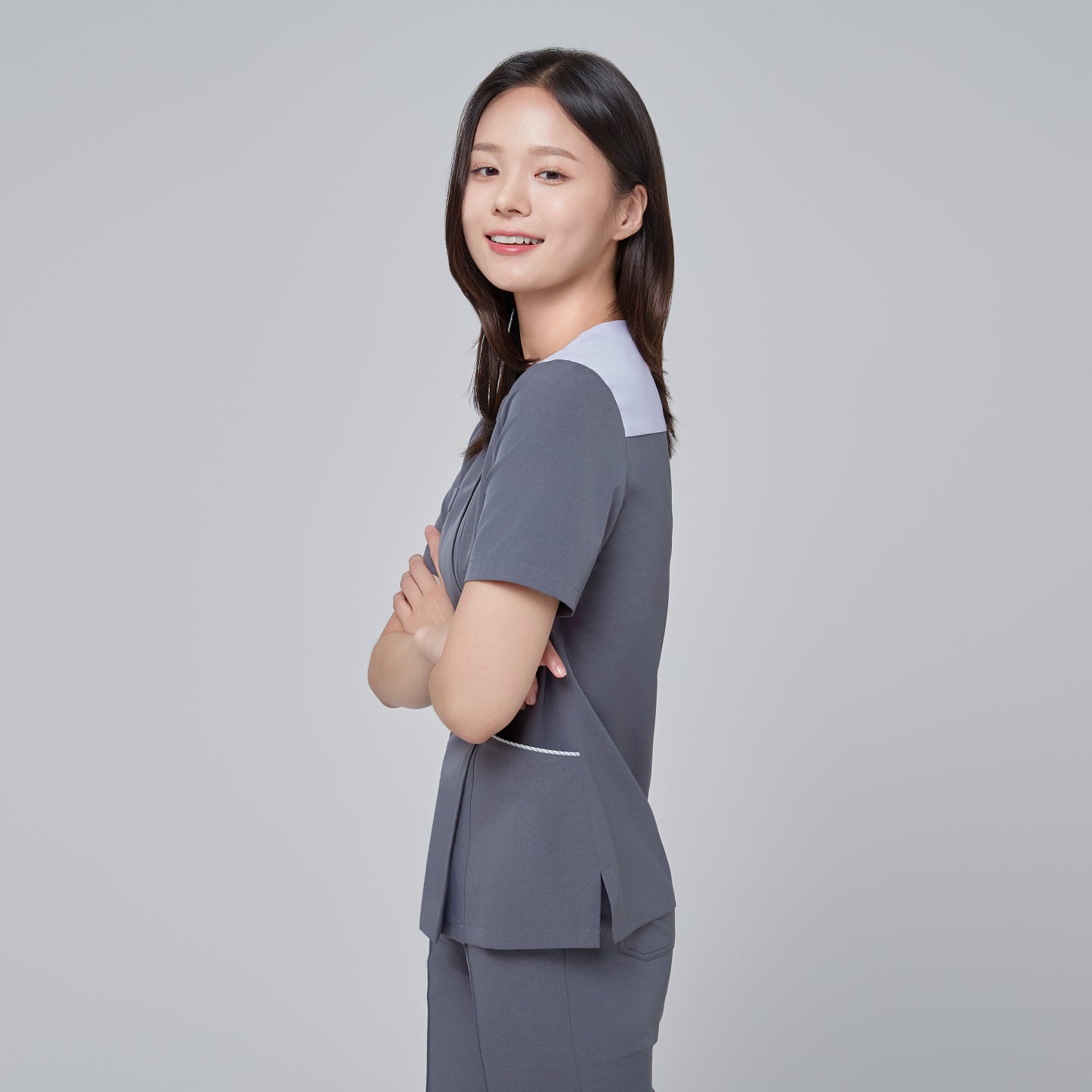 Image of Side angle of TUL OS-202 Women's One Button Front Zipper Scrub Top in Blue Gray worn by a model, highlighting the smooth fabric drape, slim fit, and design details of the one-button and zipper closures.