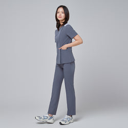 Image of Side view of TUL OS-202 Women's One Button Front Zipper Scrub Top in Blue Gray on a model, emphasizing the streamlined silhouette, the gradual drape of the fabric, and the alignment of the one-button closure with the vertical zipper detail.