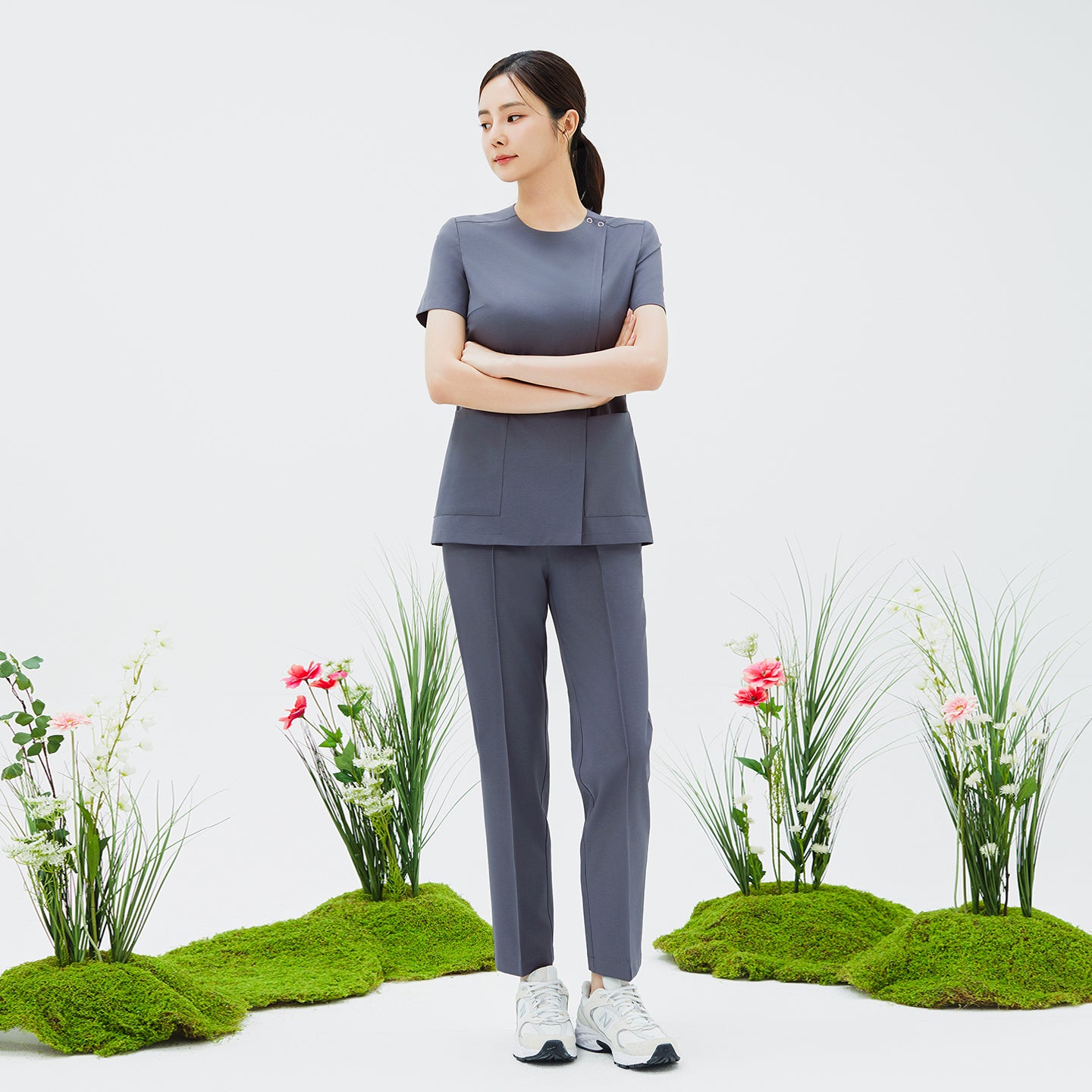 Full-length shot of TUL Women's Premium Banding Pants in Blue Gray, paired with a matching scrub top against a nature-inspired backdrop.