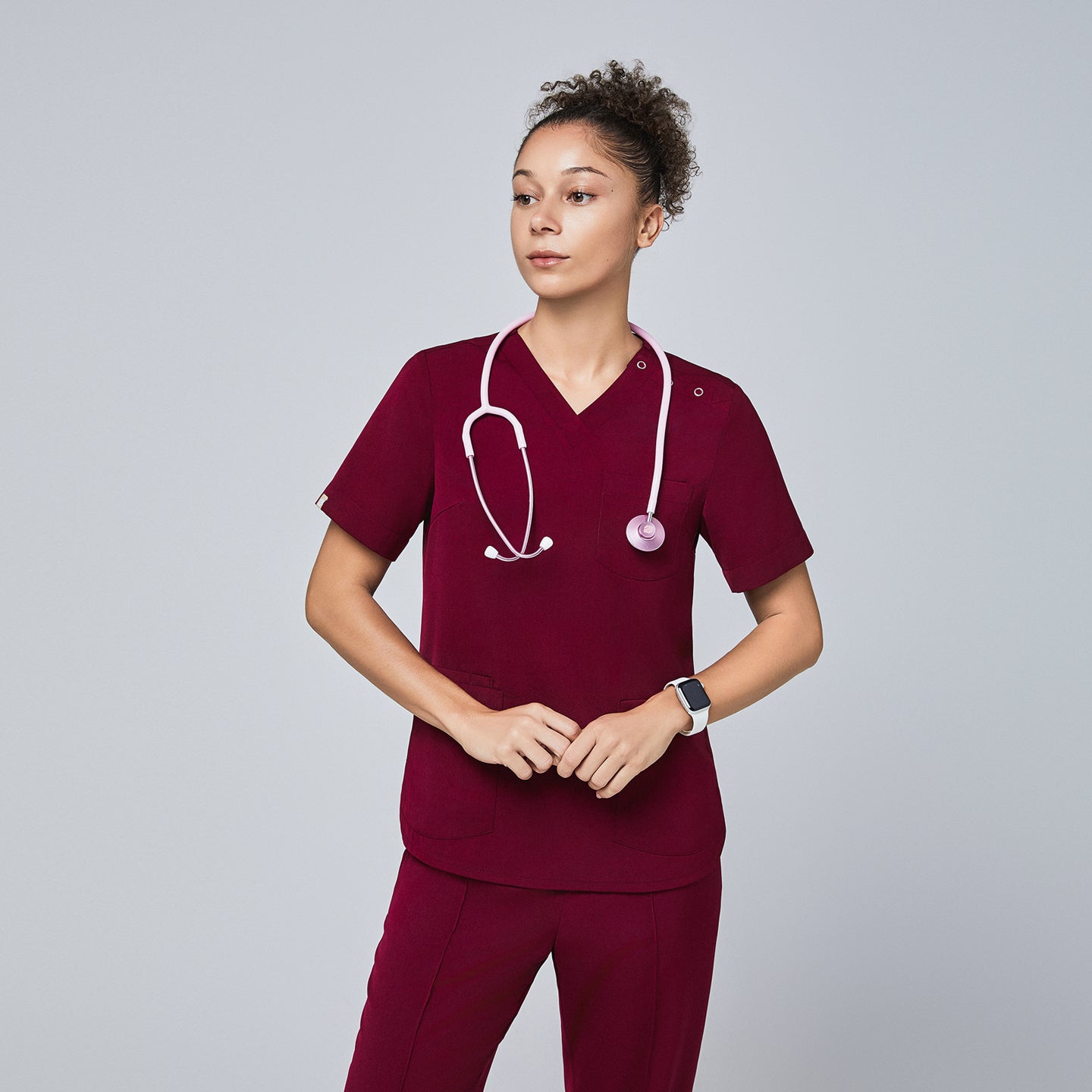 Image of Model in burgundy V-neck scrub top with three-button detail, pink stethoscope, and matching pants,Burgundy