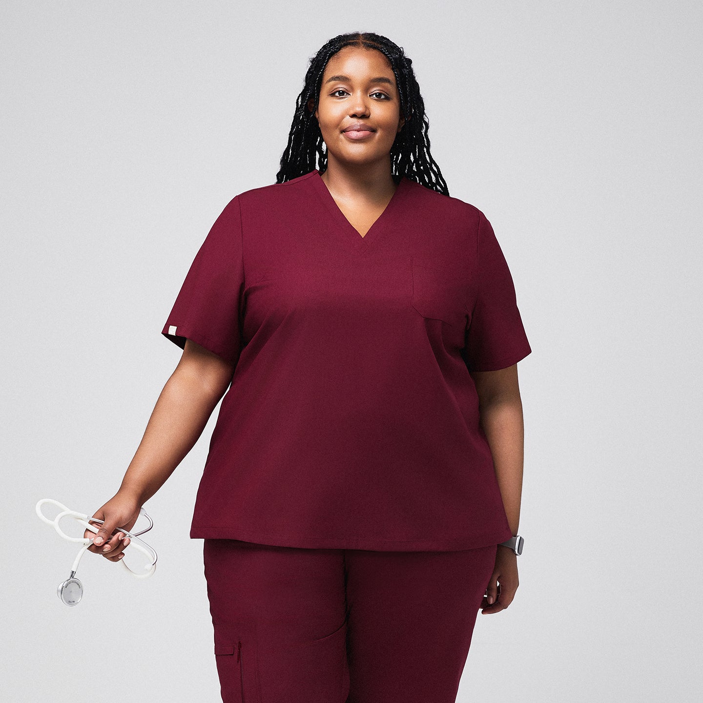 Image of Woman wearing a burgundy scrub top and matching pants, holding a stethoscope,Burgundy
