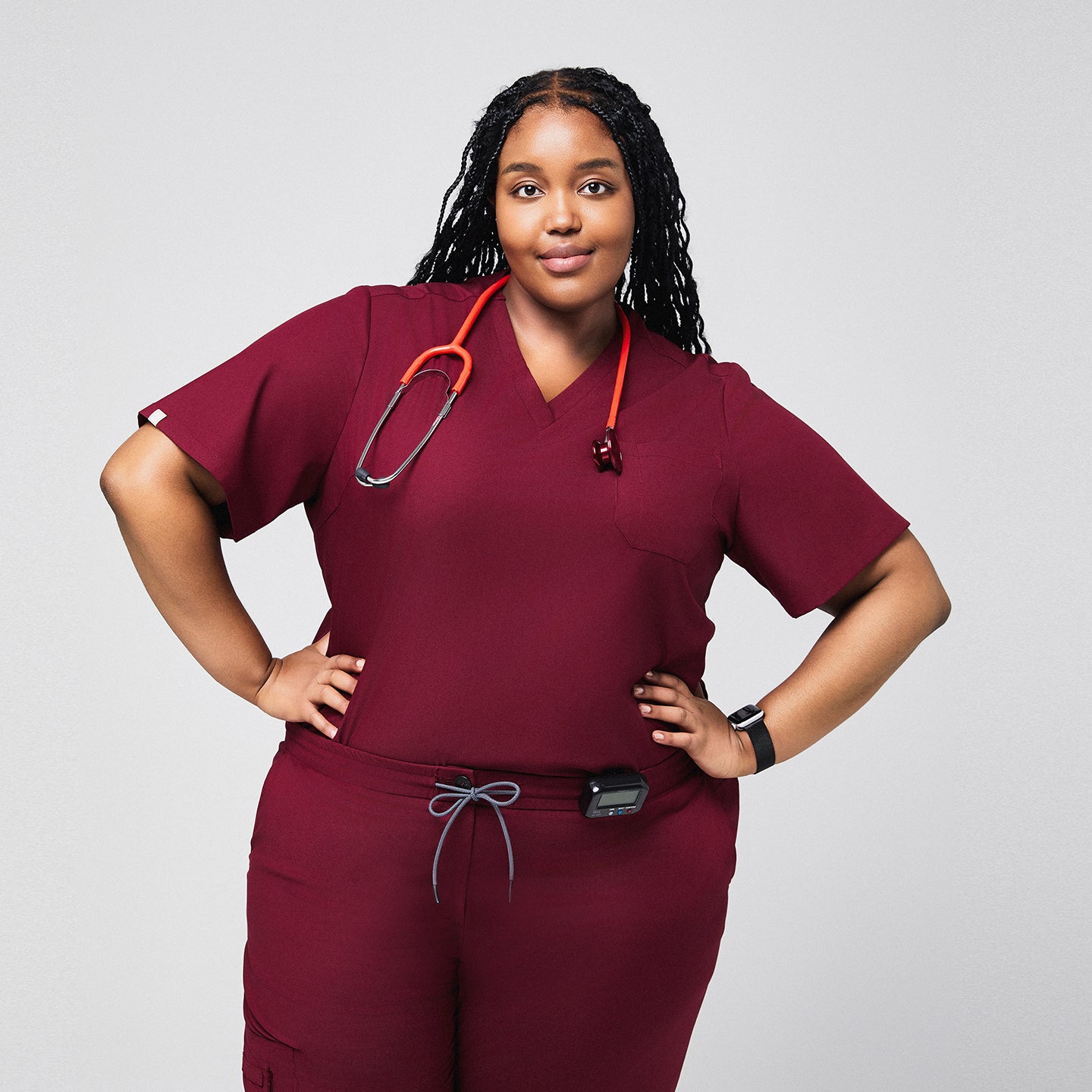 Image of Woman in a burgundy scrub set with a stethoscope around her neck, posing with hands on hips,Burgundy