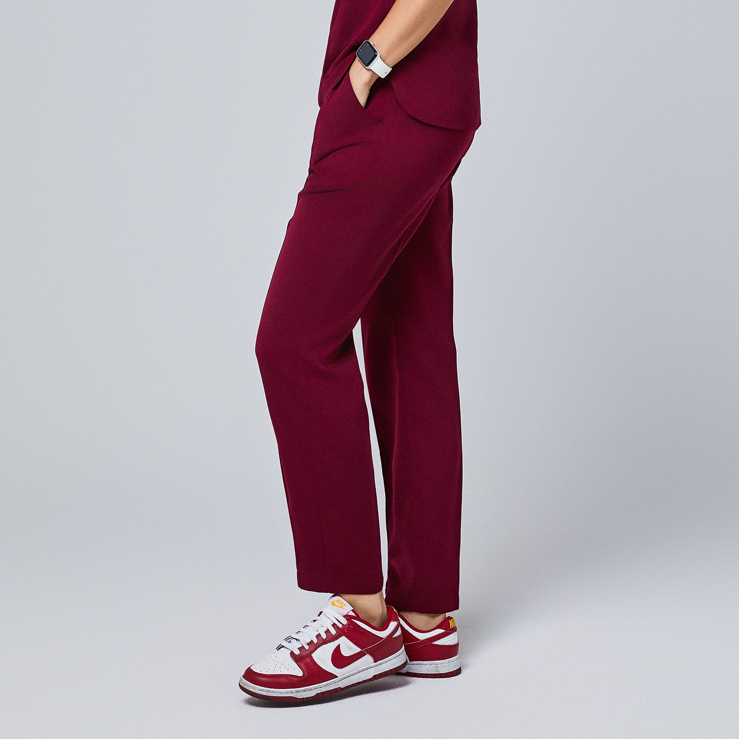 Side view of burgundy straight-leg scrub pants with a clean design, paired with red and white sneakers and accessorized with a smartwatch,Burgundy