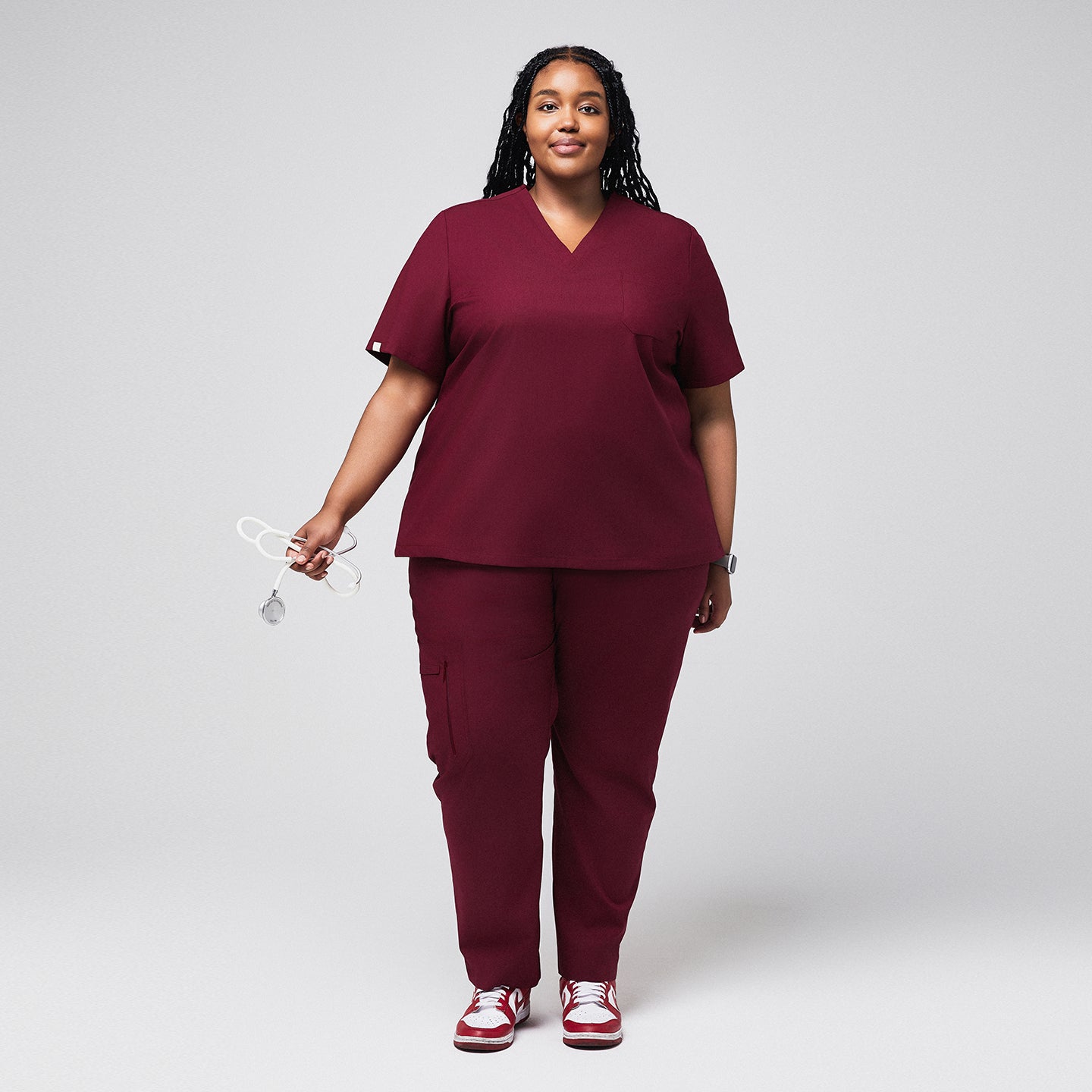 Image of Plus-size healthcare professional in burgundy scrubs with zipper pocket pants, holding a stethoscope and smiling,Burgundy