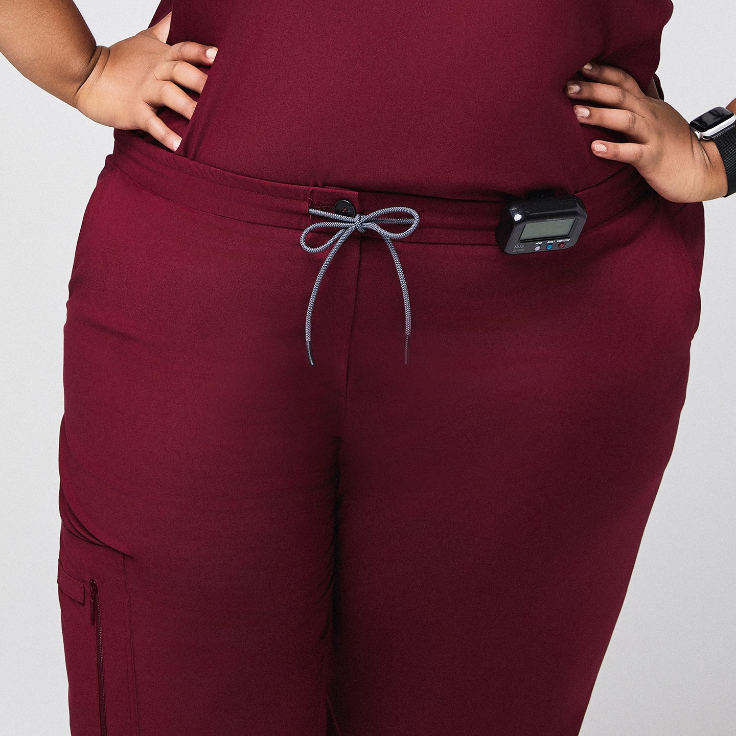 Image of Burgundy scrub pants with drawstring waist and zipper pocket, featuring a medical device clipped at the waist,Burgundy