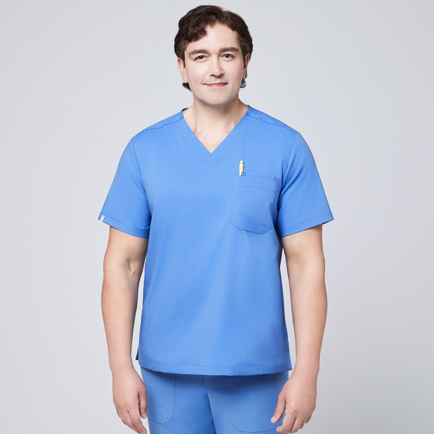 Image of Male model wearing a ceil blue V-neck scrub top with a chest pocket holding a pen, paired with matching scrub pants, designed for a professional medical setting,Ceil Blue