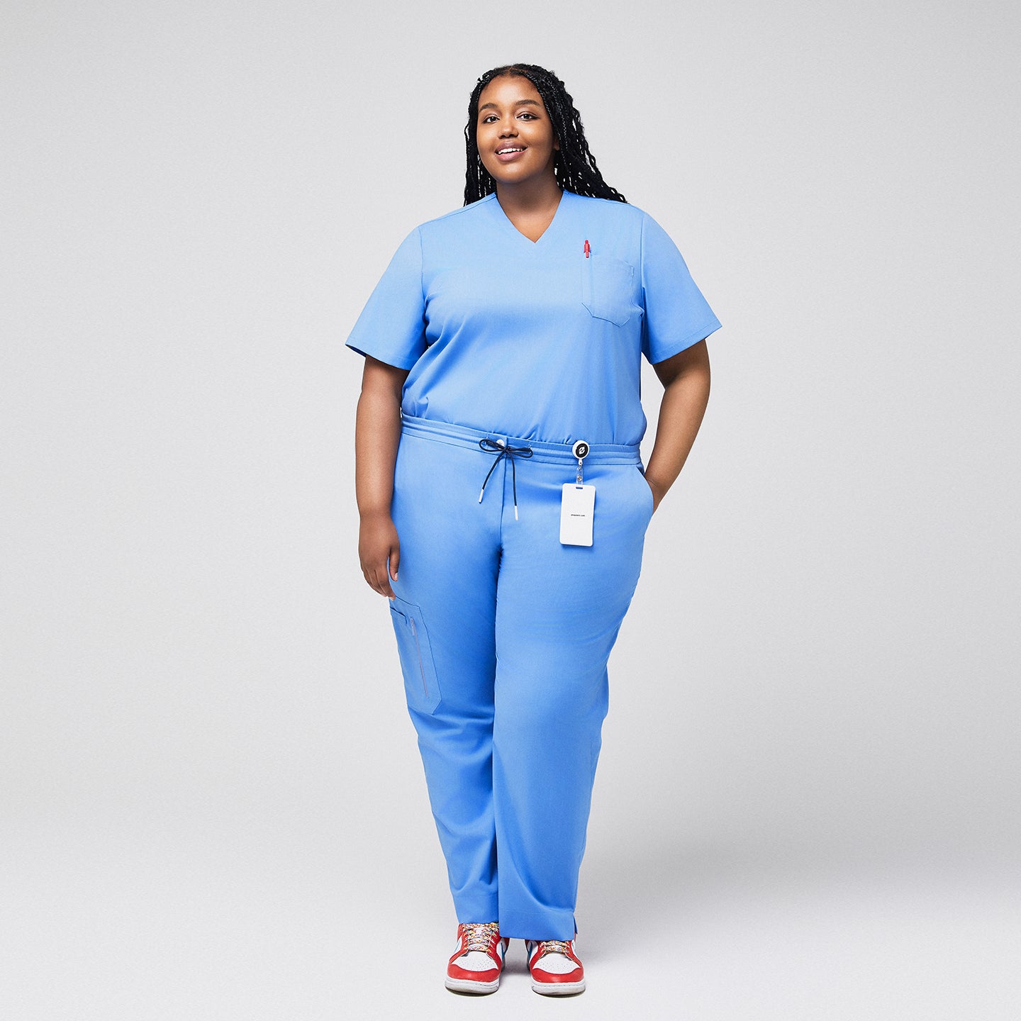 Image of Plus-size model in light blue 3-pocket scrub top with matching pants, badge holder, and red sneakers, ideal for healthcare professionals,Ceil Blue