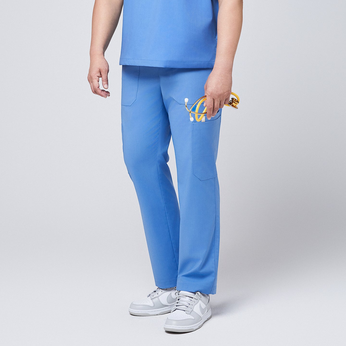 Image of Side view of a person wearing ceil blue straight scrub pants featuring utility pockets, styled with white sneakers and holding a yellow stethoscope,Ceil Blue