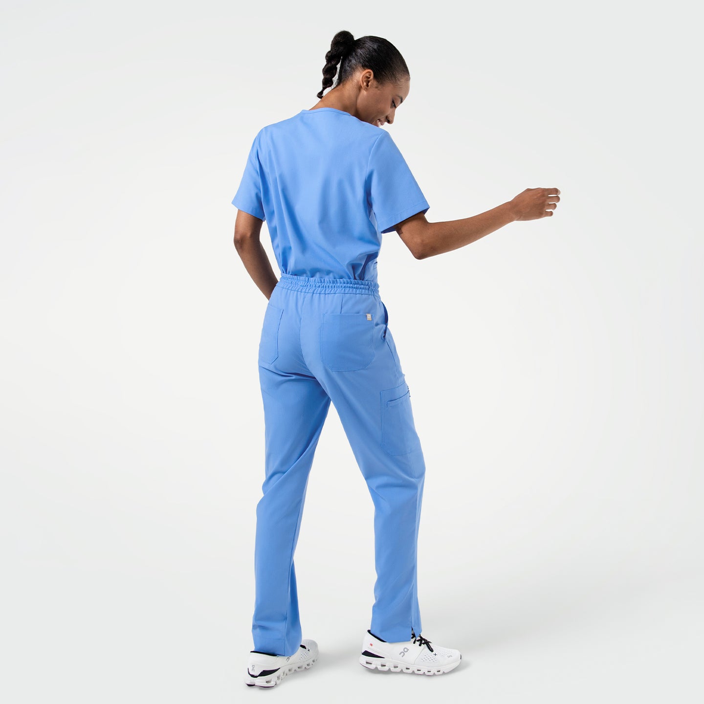Wearing the Women's Ceil Blue Double Pocket Scrub Top, walking forward with back facing the camera, full body shot