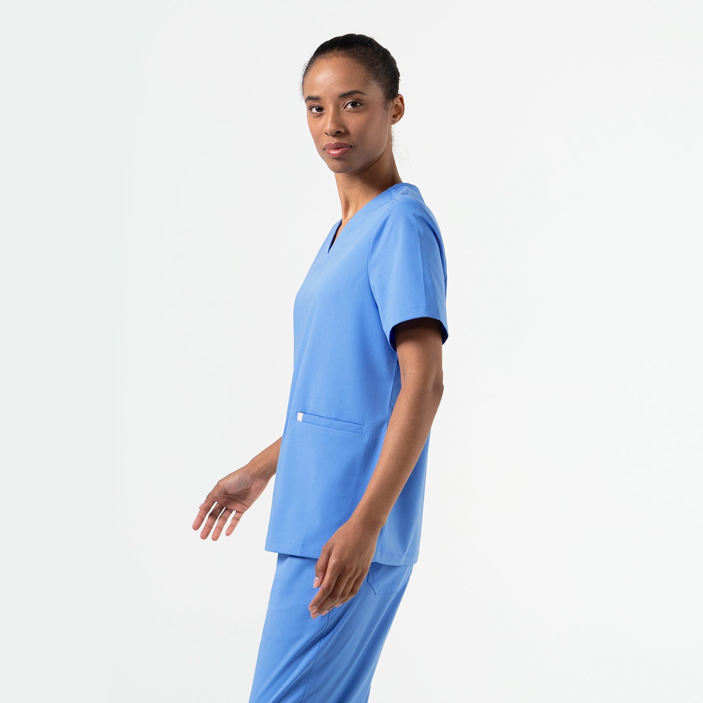 Woman wearing a Ceil Blue double-pocket scrub top, shown from a side angle with hands relaxed by her sides