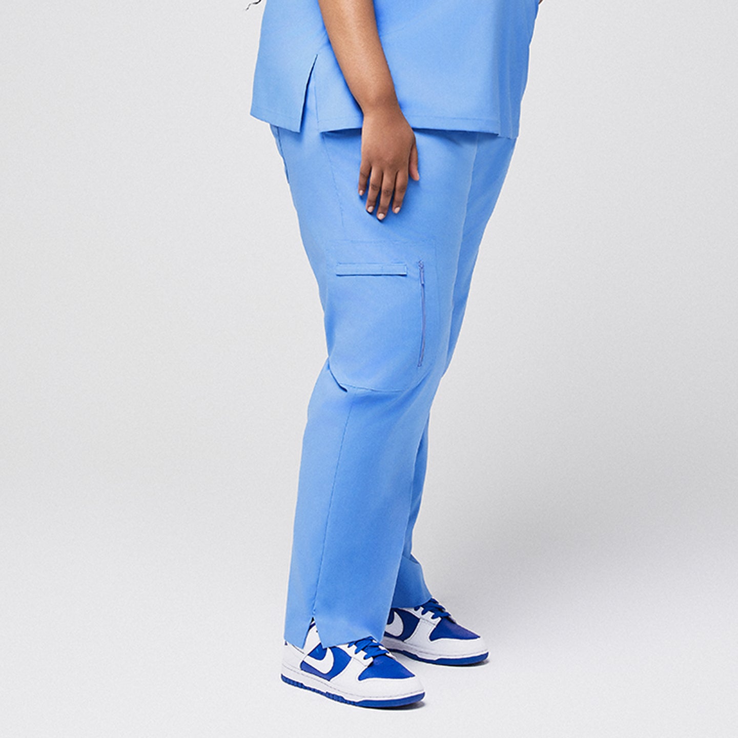 Image of Blue scrub pants with zipper pocket and split hem, side view paired with blue sneakers,Ceil Blue