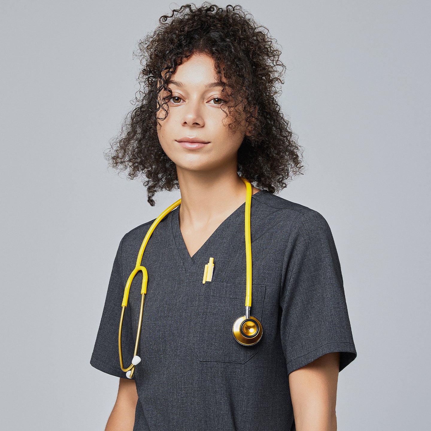 Image of Close-up of a model wearing Zenir charcoal gray 3-pocket scrub top with a yellow stethoscope,Charcoal Gray