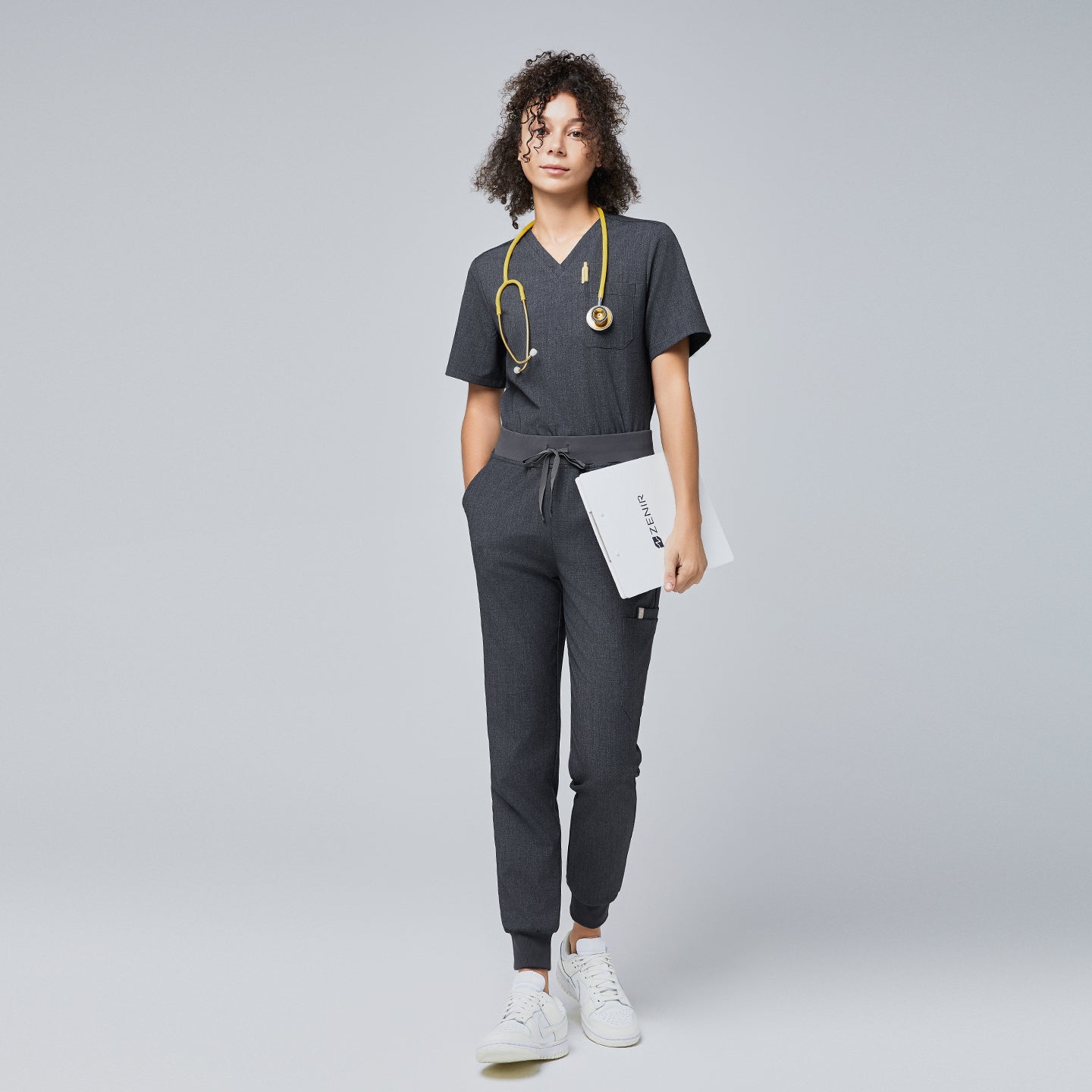 Image of Woman wearing a charcoal gray scrub set with a drawstring waist, holding a folder, and a yellow stethoscope around her neck, paired with white sneakers,Charcoal Gray