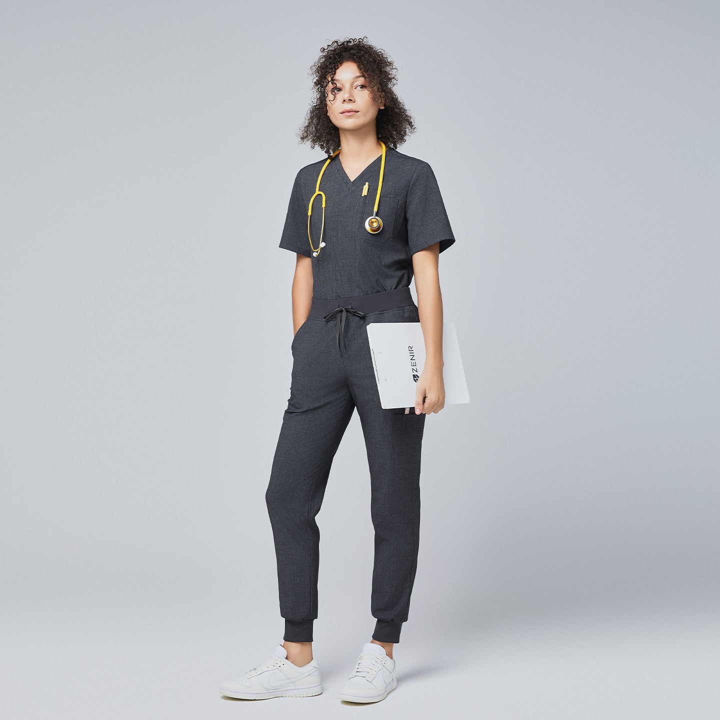 Image of Full-body view of a model wearing Zenir charcoal gray scrub set with a yellow stethoscope and holding a clipboard,Charcoal Gray