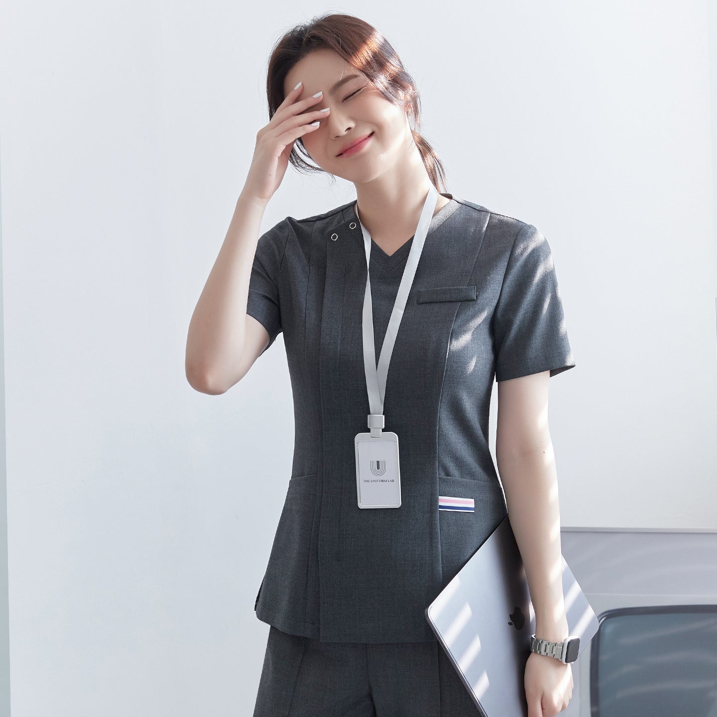 Model wearing TUL OS-182 Charcoal Gray scrub top, highlighting the front zipper closure and chest pocket.