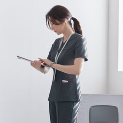 Image of Side view of TUL OS-182 Women's Front Zipper Scrub Top in Charcoal Gray, worn by a model holding a tablet.