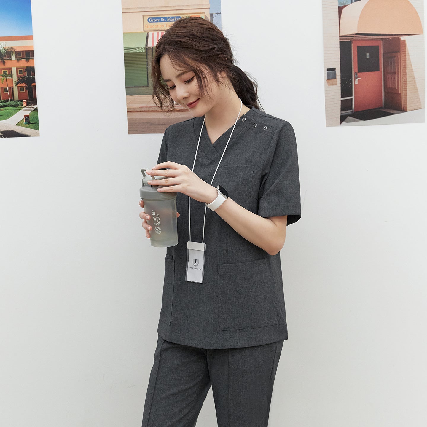 Model in TUL OS-186 Women's Charcoal Gray scrub top, showing snap button closures near the shoulder and large front pockets.