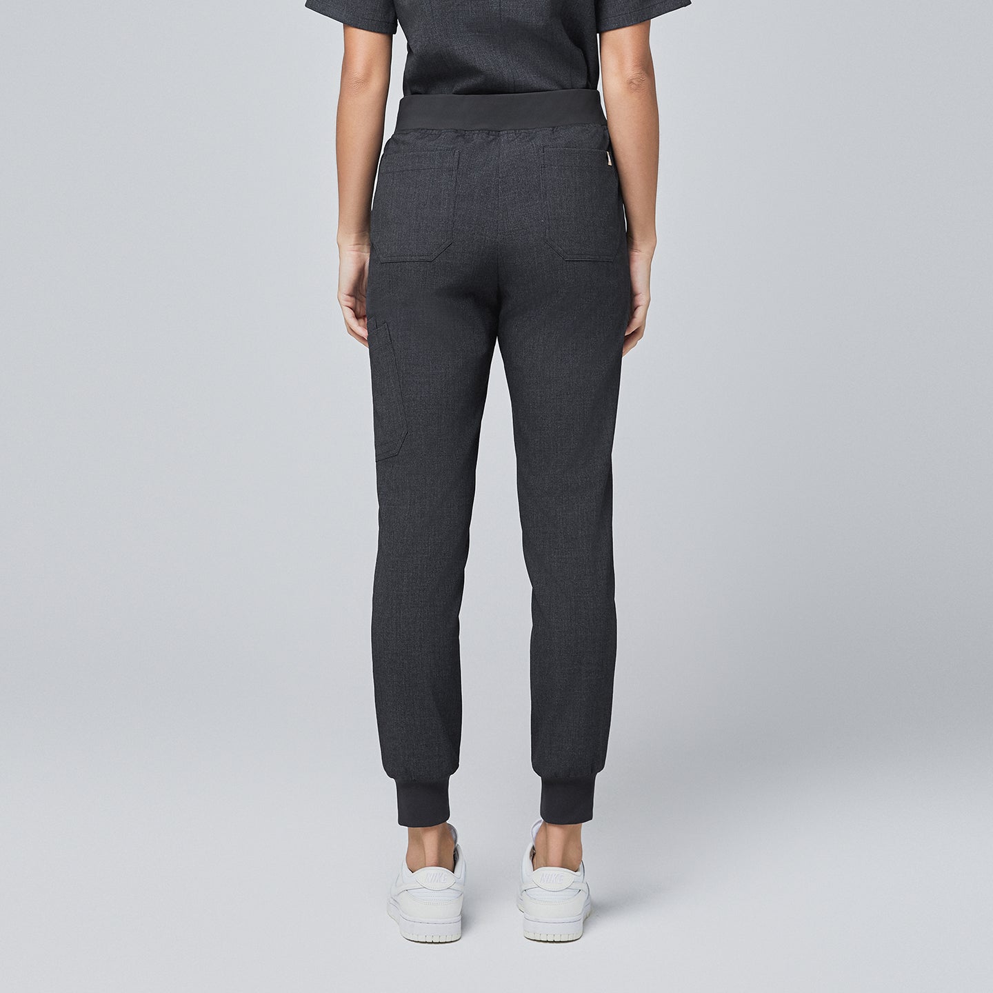 Image of Back view of charcoal gray jogger scrub pants with rear pockets, elastic waistband, and cuffed ankles, paired with white sneakers,Charcoal Gray