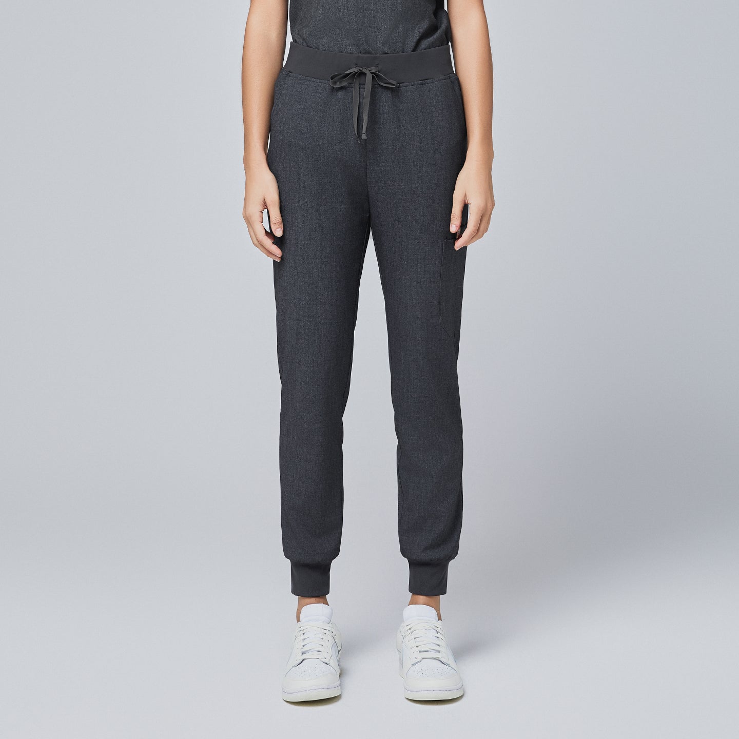 Image of Front view of charcoal gray jogger scrub pants with an elastic waistband, adjustable drawstring, and cuffed ankles, paired with white sneakers,Charcoal Gray