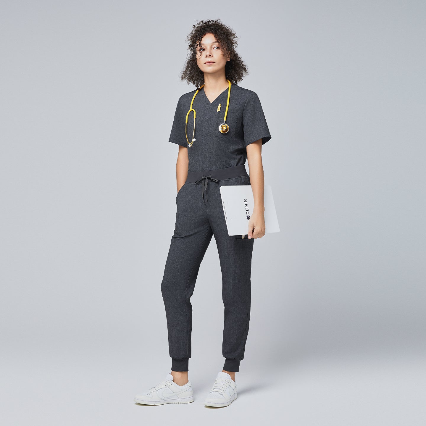 Image of Full-body view of a woman wearing charcoal gray jogger scrub pants and matching top, accessorized with a yellow stethoscope and holding a clipboard,Charcoal Gray