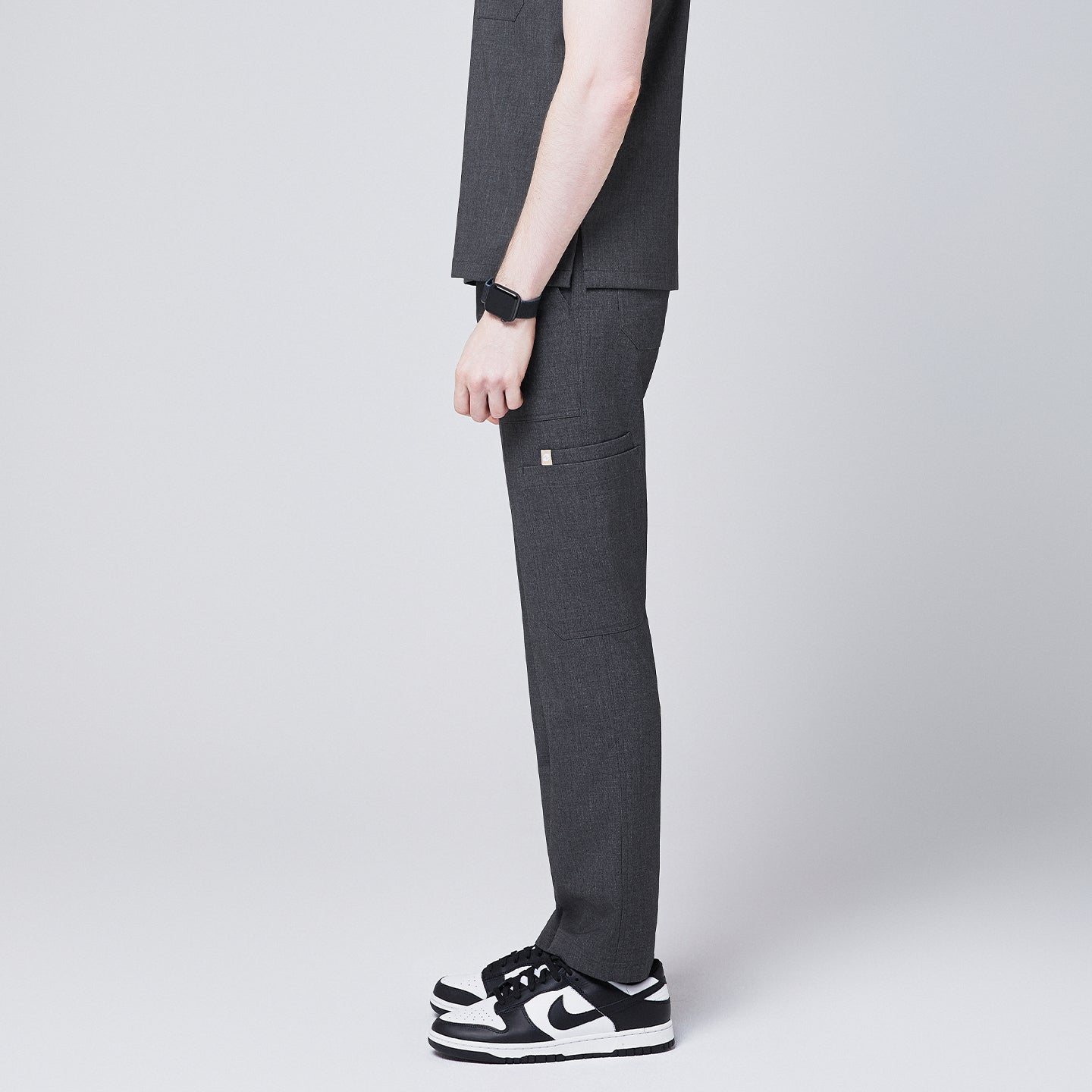 Image of man showcasing the side view of Zenir charcoal-gray zipper straight scrub pants, paired with black-and-white sneakers and a smartwatch,Charcoal Gray
