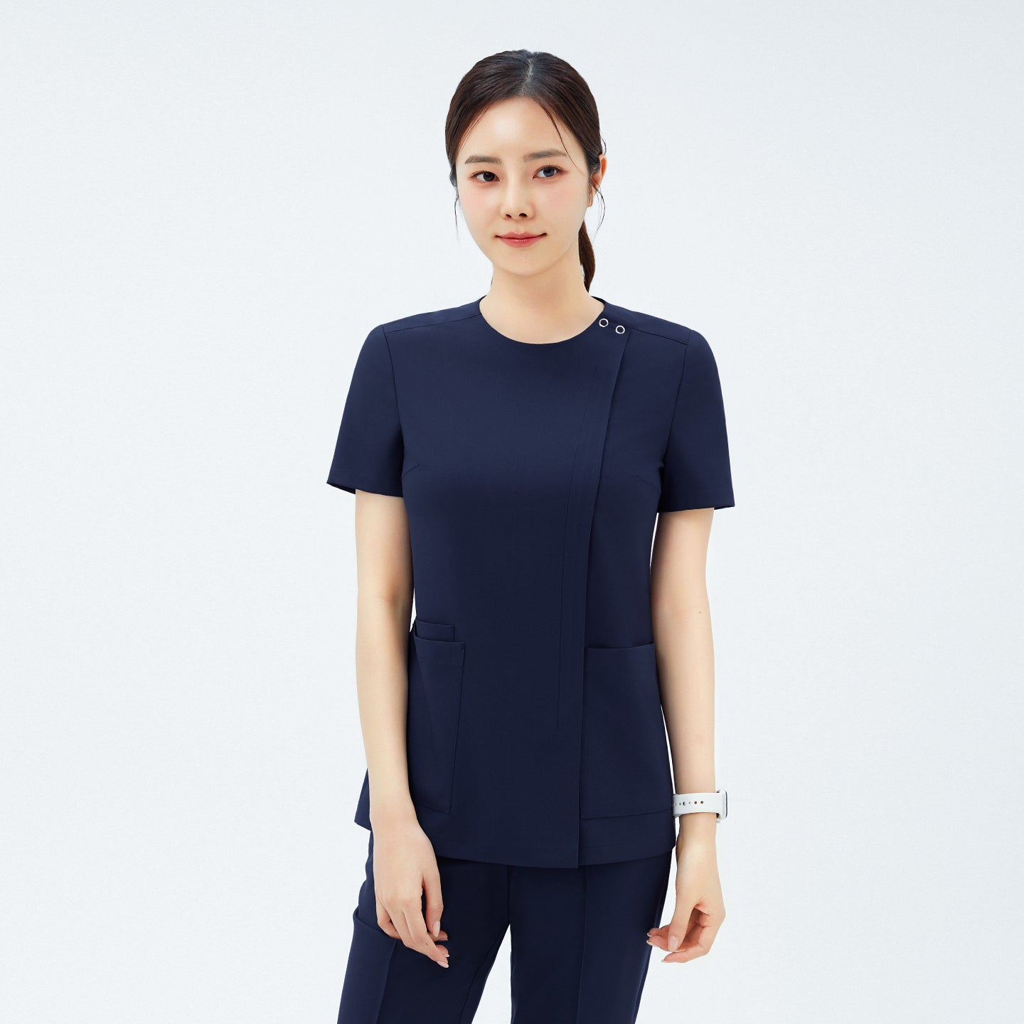 Model wearing TUL OS-213 Women's Dual Snap Front Zipper Scrub Top in Classic Navy, showing snap button detail at the neckline and front pockets.