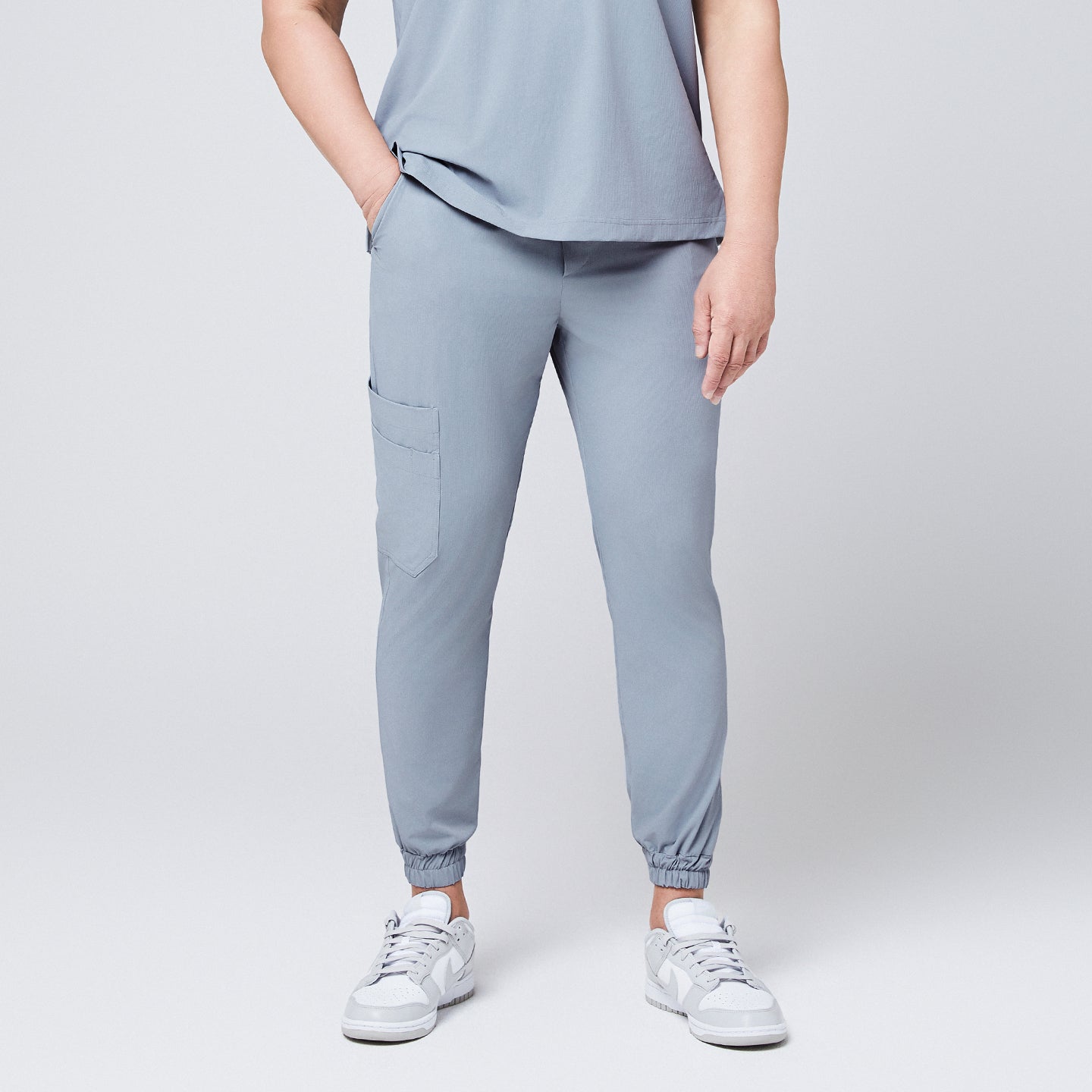 Image of Front view of cool gray jogger scrub pants with a cargo pocket and elastic cuffs, paired with gray Nike sneakers,Cool Gray