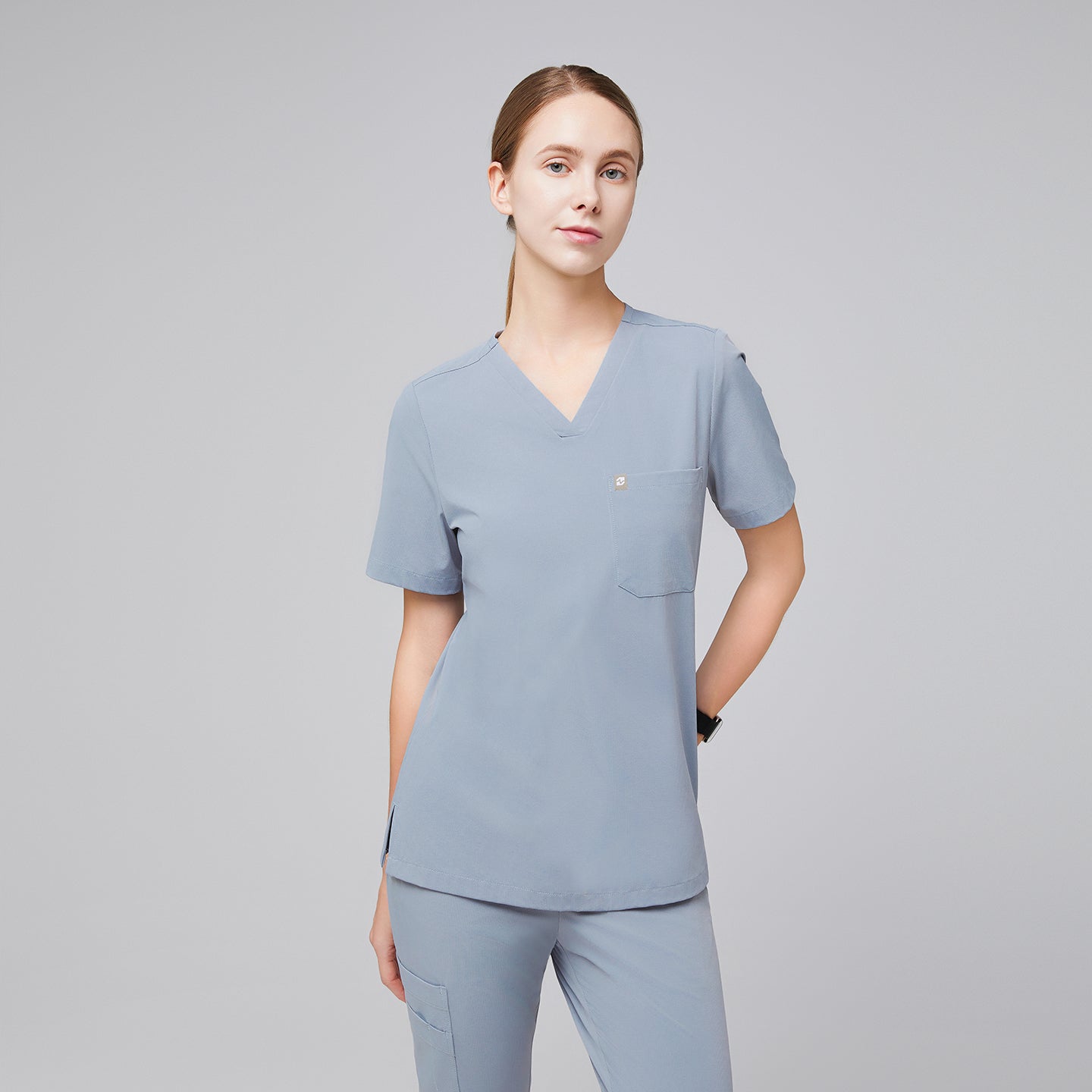 Image of Female healthcare professional in a cool gray scrub top and pants, adjusting the hem of the top,Cool Gray